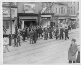 Photograph of civilians and servicemen standing outside of smashed shop windows on Barrington Str...