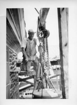 Photograph of a man lifting something with chains and pulleys