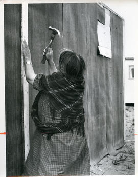 Photograph of Alicie Berthé hammering a nail into her house