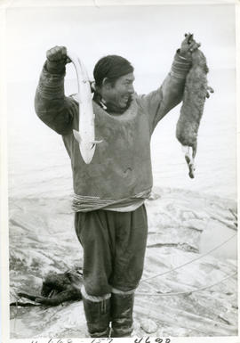 Photograph of Stan Annanak holding a fish and a rabbit near Ungava Bay