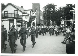 Photograph of a parade of Canadian Armed Forces and a military band marching down a street in Hol...