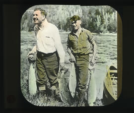 Photograph of two unidentified men carrying fish from a canoe