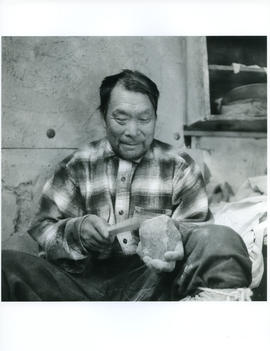 Photograph of an unidentified man working with a tool and a rock