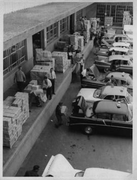 Photograph of people loading telephone directories into the trunks of Halifax taxi cabs