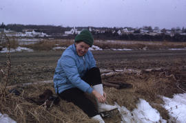 Photograph of Barbara Hinds sitting on the ground and lacing ice skates