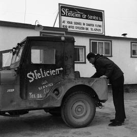 Photograph of a man looking in the back of a Jeep belonging to the St. Felicien Air Service in no...