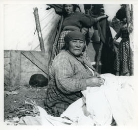 Photograph of a woman sitting on the ground near a tent in Davis Inlet, Newfoundland and Labrador