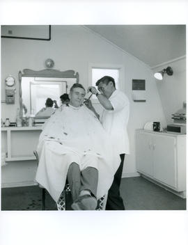 Photograph of an unidentified man having his hair cut by a barber