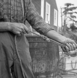 Photograph of an unidentified man tying a knot in a rope