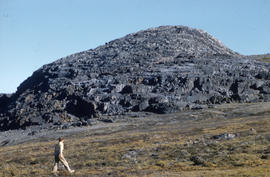 Photograph of a woman walking by a large rock formation in the eastern Canadian Arctic
