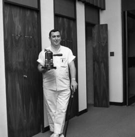 Photograph of an unidentified person with a coffee pot and a walking stick