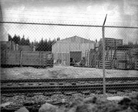 Photograph of crates and railroad tracks behind a fence