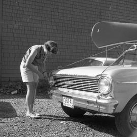 Photograph of an unidentified woman tying a canoe to the roof of a car