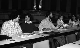 Photograph of five unidentified people sitting at desks