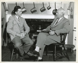 Photograph of Thomas Head Raddall holding a book and speaking with CBC interviewer Lloyd MacInnis...