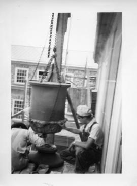 Photograph of men lifting a stone stulpture with chains