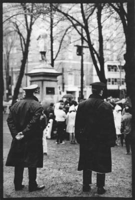 Photograph of two police officers standing behind a group of protesters listening to speakers at ...