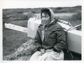 Photograph of a woman carrying pieces of a packing case with a harness in Fort Chimo, Quebec