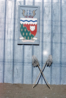 Photograph of the Northwest Territories crest and two mops on the side of a building in Frobisher...