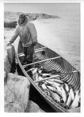 Photograph of an unidentified man standing in a boat full of fish