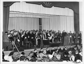 Photograph of scientists and guests on stage gathered around Chancellor C.D. Howe