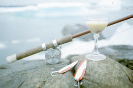 Photograph of a fishing rod, a glass, and fish hooks