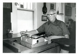 Photograph of Thomas Head Raddall sitting at his desk with a typewriter