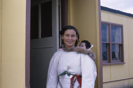 Photograph of Joanna Koneak standing in a doorway while carrying a baby on her back