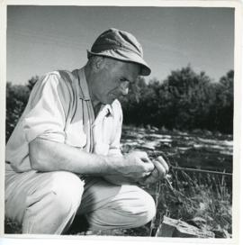 Photograph of Thomas Head Raddall untangling a fishing lure near Trout Rock, at the foot of Lake ...