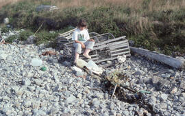 Photograph of one unidentified person sitting on a littered lobster track on the rocky shore of B...