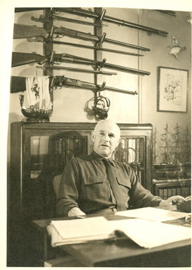 Photograph of Thomas Head Raddall captured mid-speech, sitting at his desk in his study
