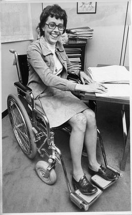 Photograph of Constance Glube sitting in a wheelchair at a desk