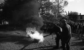 Photograph of an unidentified person putting out a fire with a fire extinguisher