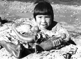 Photograph of a child with three carvings of a sea goddess