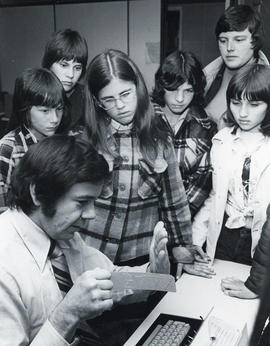 Photograph of a man showing a computer punch card to a group of children