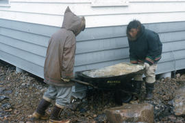 Photograph of two people moving a stone with a wheelbarrow
