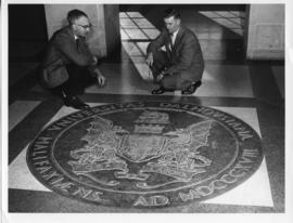 Photograph of two men with the bronze seal in the Arts & Administration Building