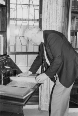 Photograph of a man looking at a book in the Kipling room at the MacDonald Library