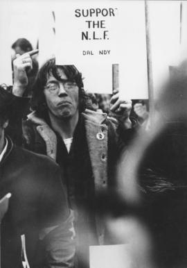 Photograph of Will Offley pointing to his "Support the N.L.F." (National Liberation Front) sign d...