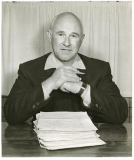 Portrait of Thomas Head Raddall in his study, marking a stack of papers