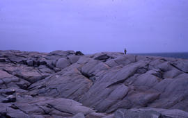 Photograph of a landscape of giant rocks by the water with an unidentified man standing on top