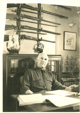 Photograph of Thomas Head Raddall sitting at his desk in his study