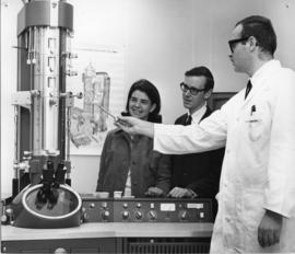 Photograph of Morley Bleviss showing an electron microscope to two attendees at an open house