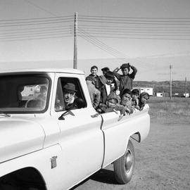 Photograph of Canon James Clarke driving pickup truck with several children in the back in Fort C...