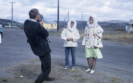 Photograph of two young women wearing white parkas and being filmed by a man