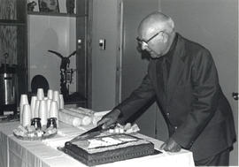 Photograph of Thomas Head Raddall cutting a cake at the first birthday of the Perkins House Museu...