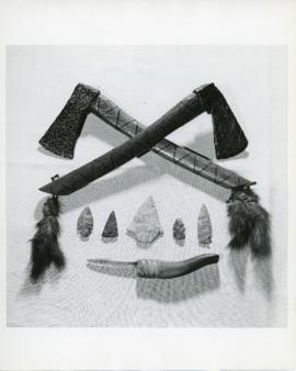 Photograph of two iron hatchets or tomahawks decorated with feathers, five stone arrowheads, and ...
