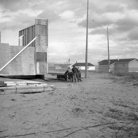 Photograph of three people moving a section of a house in Fort Chimo, Quebec