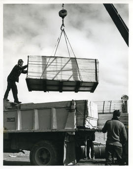 Photograph of a crate being loaded onto a truck with a crane