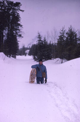 Photograph of Les Cwynar leaning on snowshoes on a snow-covered road, northern Ontario